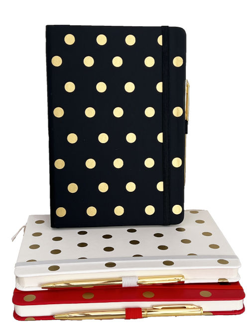 Stacked A5 notebooks with large gold dot covers and matching gold pens, with one notebook standing upright.