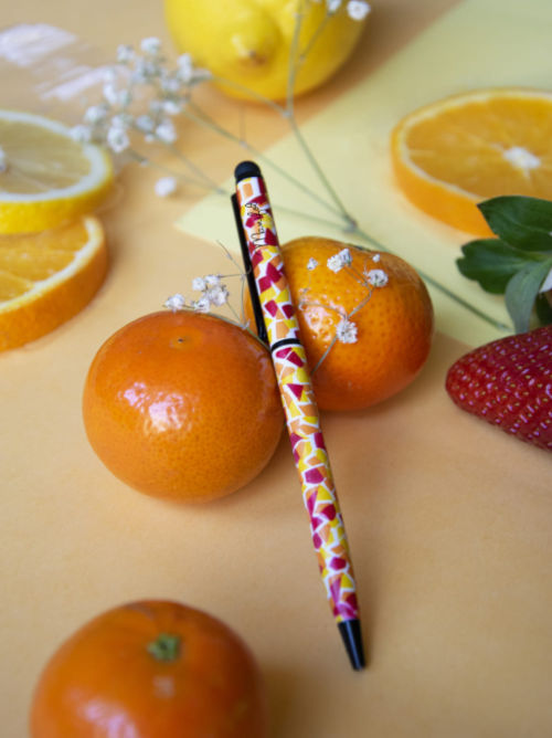 Mosaic-patterned ballpoint pen with stylus tip placed on a surface with citrus fruit and soft natural elements