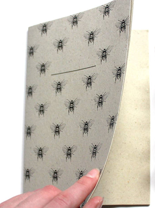 Slightly open image of the wild bee grass paper notebook, covered in bees showing plain grass paper interior. 