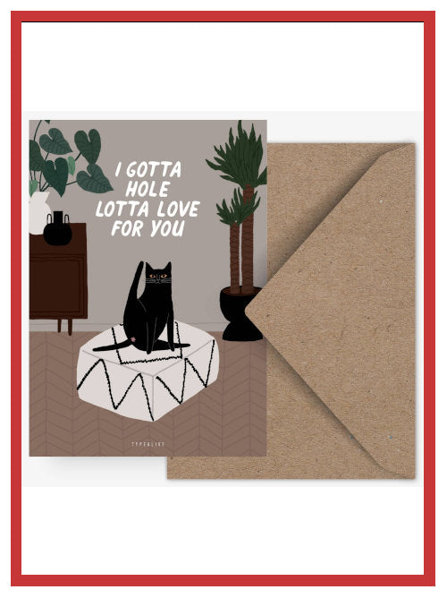 Funny Valentine postcard showing black cat sitting on pouffe with the words “I gotta hole lotta love for you”, displayed with kraft envelope