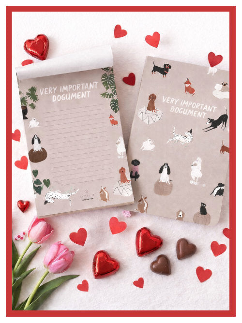 Dog illustrated notebook and notepad arranged on a light surface with red heart decorations and flowers