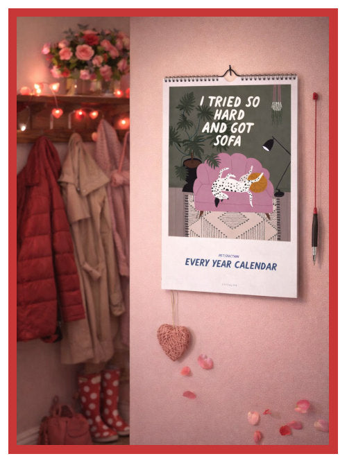 Wall calendar hanging on a hook in a hallway with coats, shoes, and Valentine’s Day decorations in the background